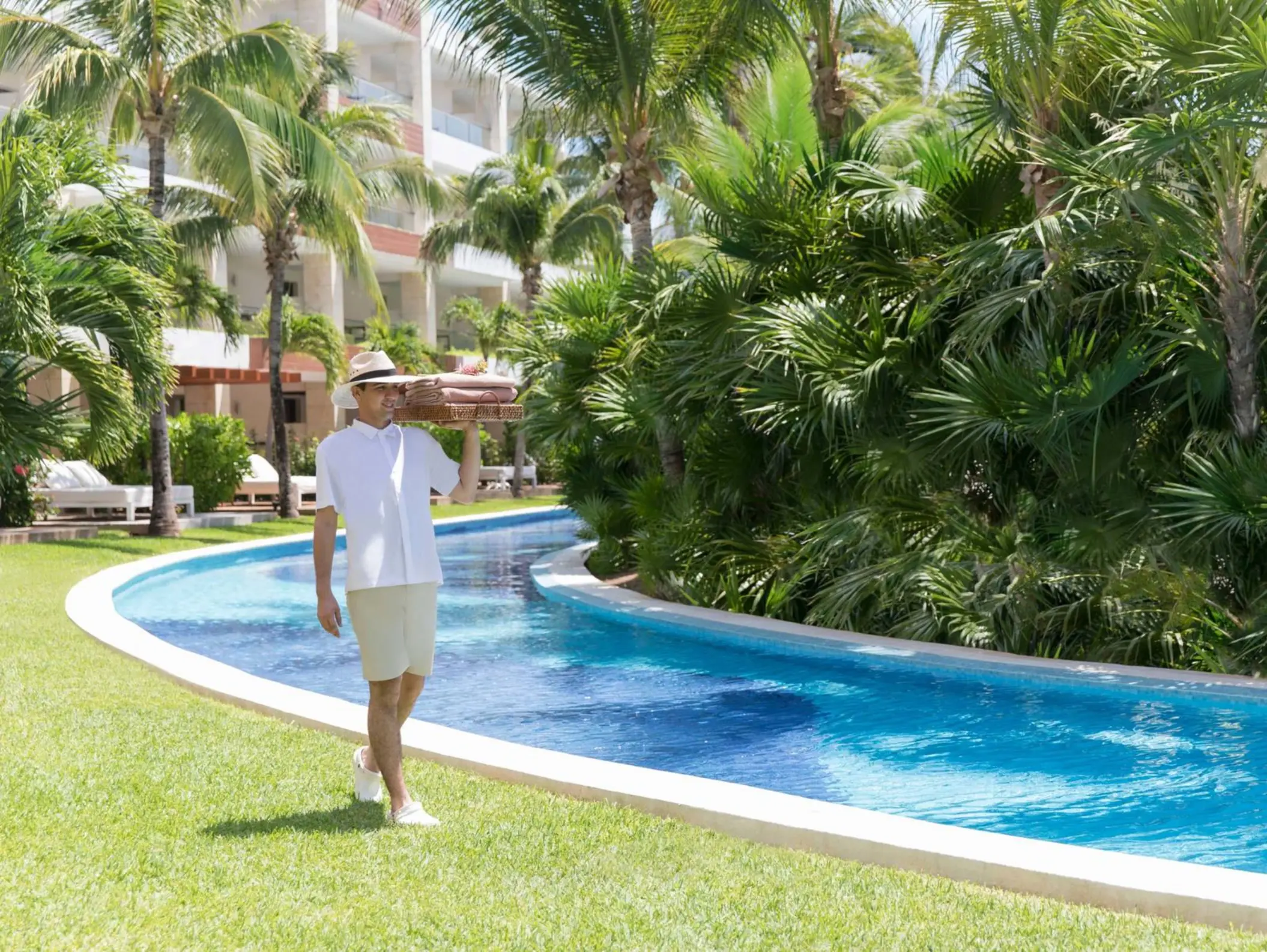 Resort staff walking by the lazy river, surrounded by tropical greenery and white buildings in the background.