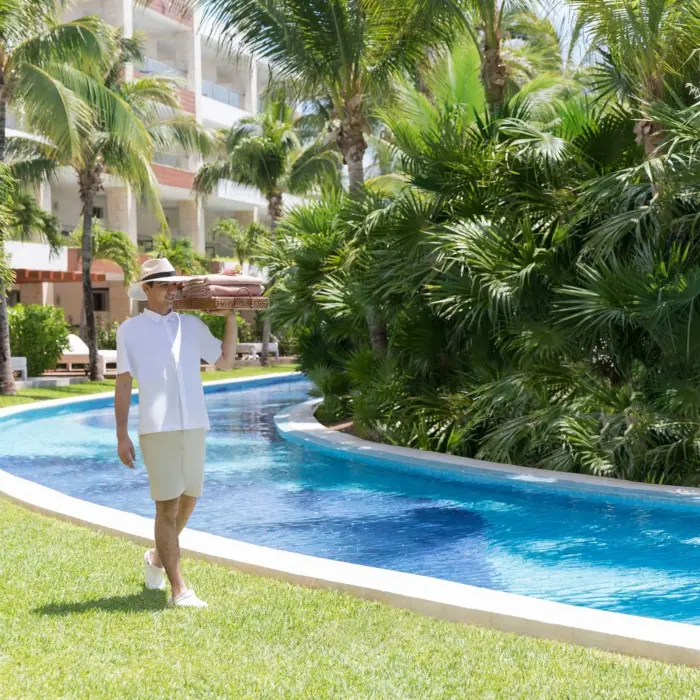 Resort staff walking by the lazy river, surrounded by tropical greenery and white buildings in the background.