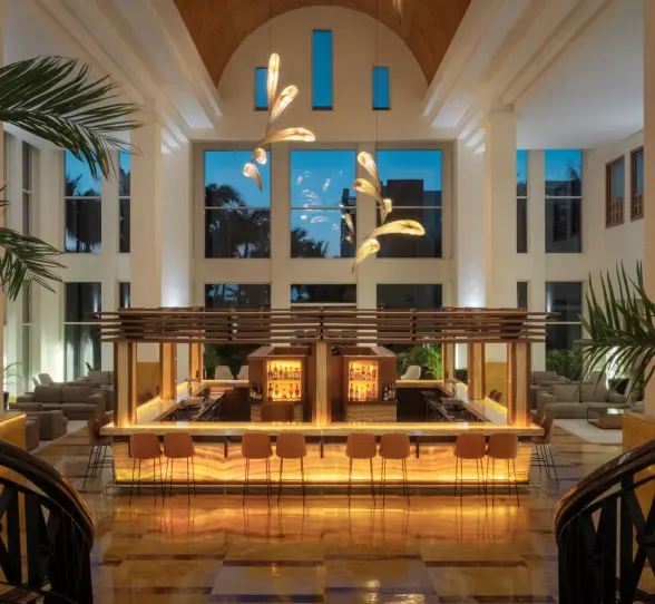 Elegant indoor lobby bar with glowing amber lighting, high ceilings, and modern chandeliers at dusk.