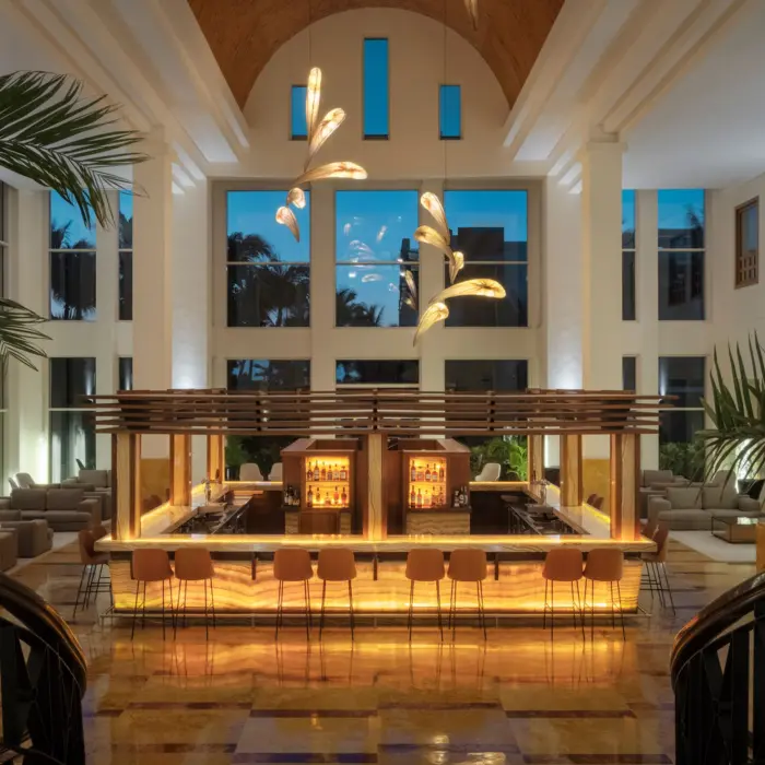 Elegant indoor lobby bar with glowing amber lighting, high ceilings, and modern chandeliers at dusk.