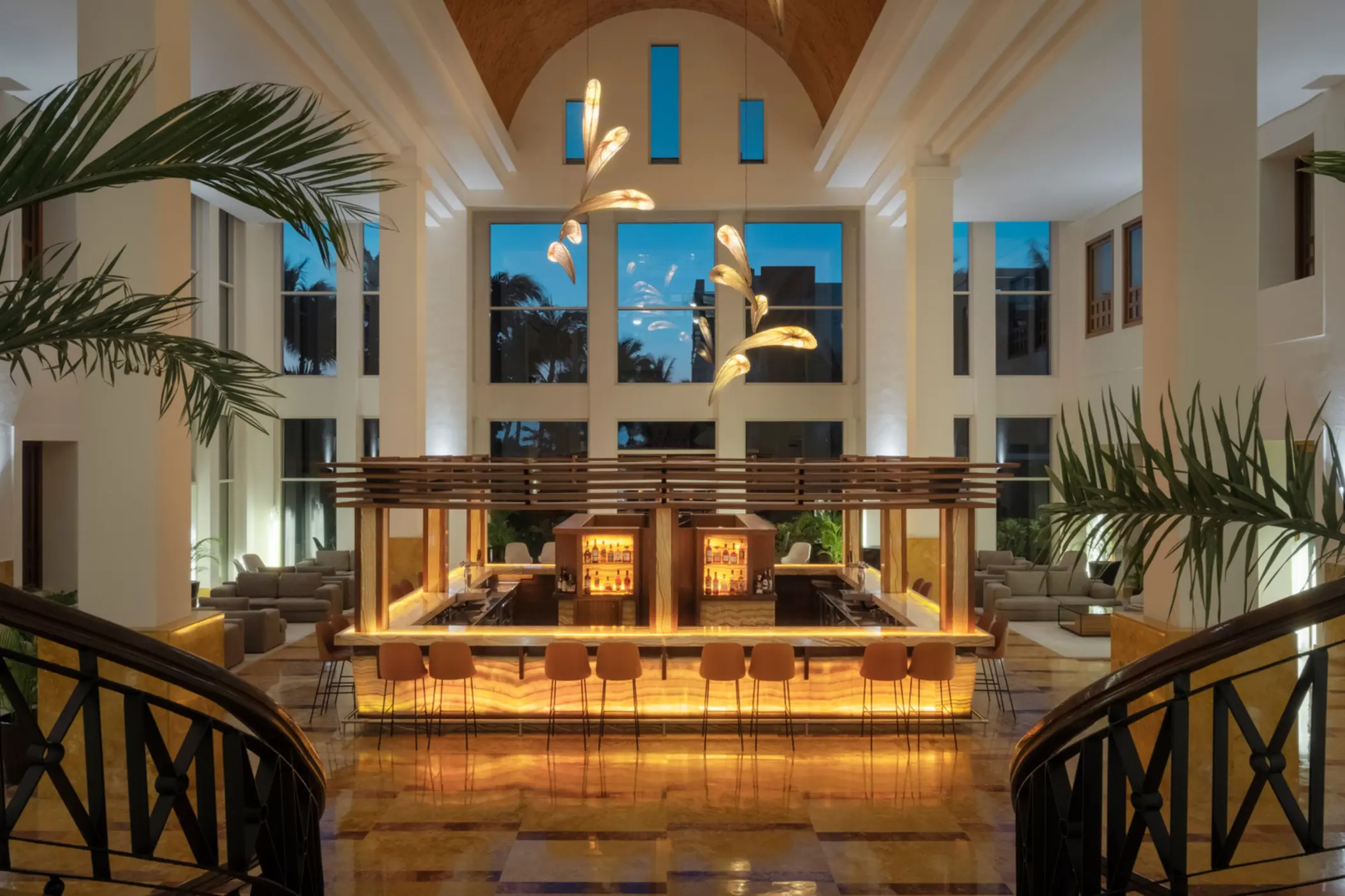Elegant indoor lobby bar with glowing amber lighting, high ceilings, and modern chandeliers at dusk.
