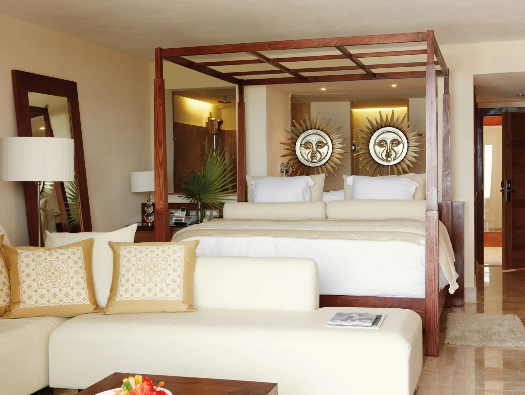 Bright, cozy suite with wooden canopy bed, sun-themed wall art, cream seating, and soft neutral tones