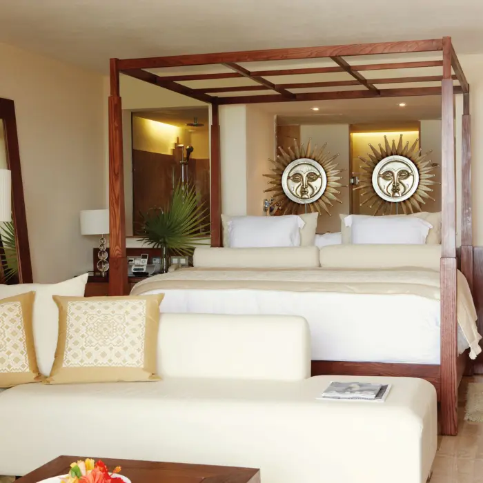 Bright, cozy suite with wooden canopy bed, sun-themed wall art, cream seating, and soft neutral tones