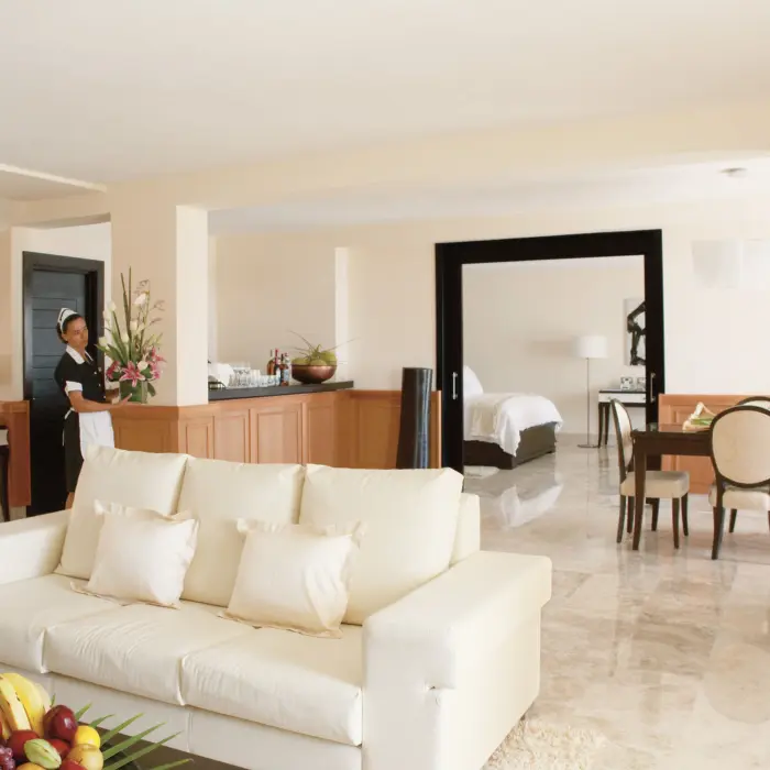 Spacious luxury suite with open layout, cream couch, dining area, fresh flowers, and a stocked minibar.