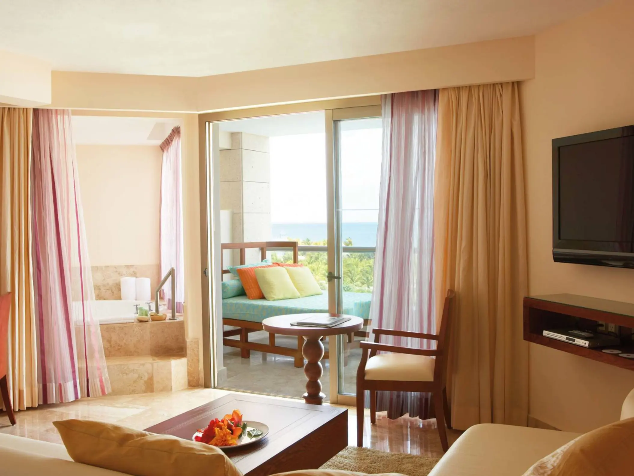 Junior suite with a private terrace, soaking tub, sheer curtains, and ocean views beyond the sliding doors.