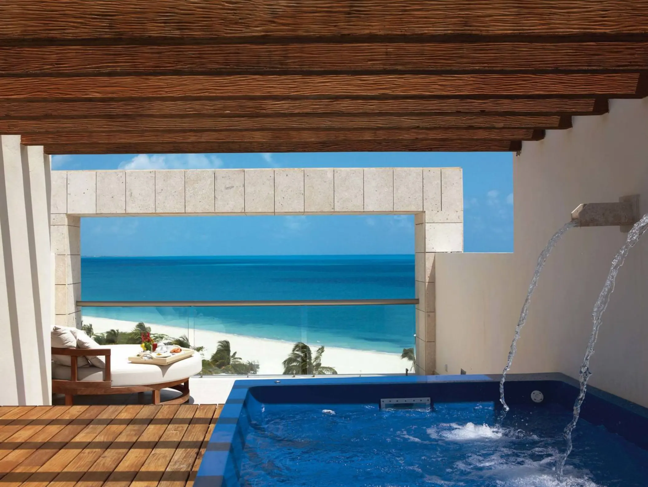 Private terrace with ocean views, wooden pergola, and a blue jacuzzi tub overlooking white sand beach below.