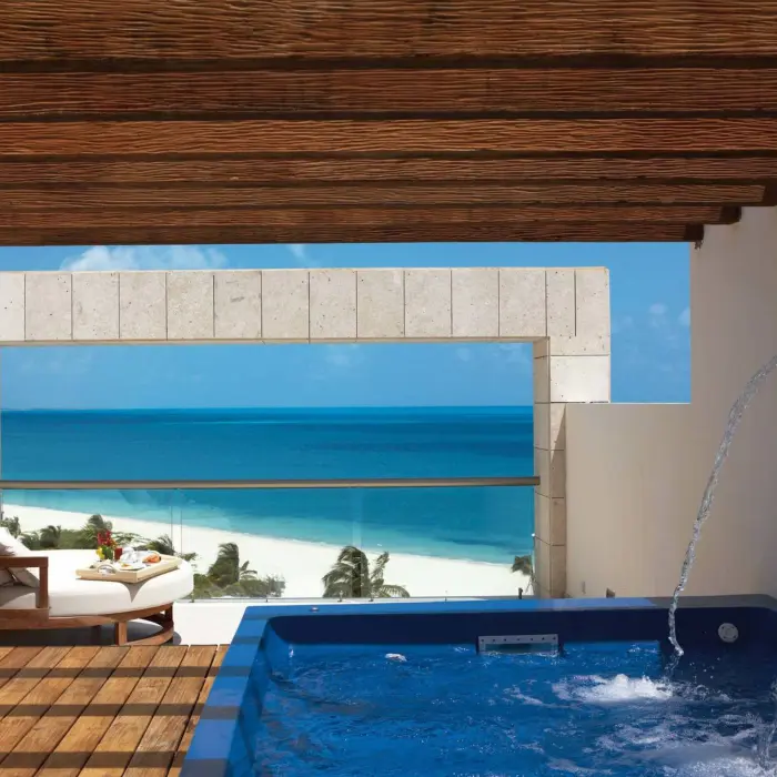 Private terrace with ocean views, wooden pergola, and a blue jacuzzi tub overlooking white sand beach below.