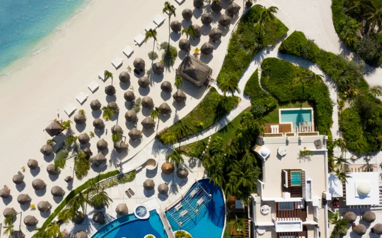 Aerial view of resort beachfront, palapas, and ocean-facing suites surrounded by greenery and soft sand.
