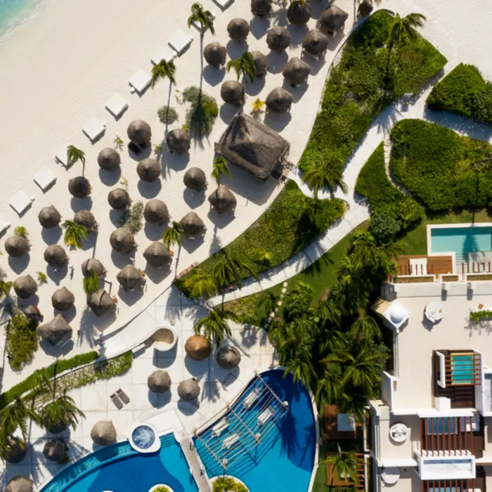 Aerial view of resort beachfront, palapas, and ocean-facing suites surrounded by greenery and soft sand.