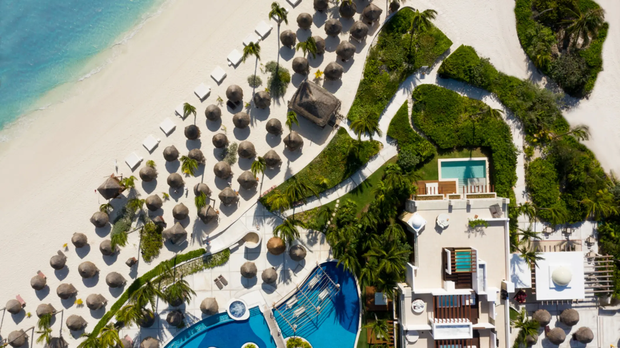 Aerial view of resort beachfront, palapas, and ocean-facing suites surrounded by greenery and soft sand.