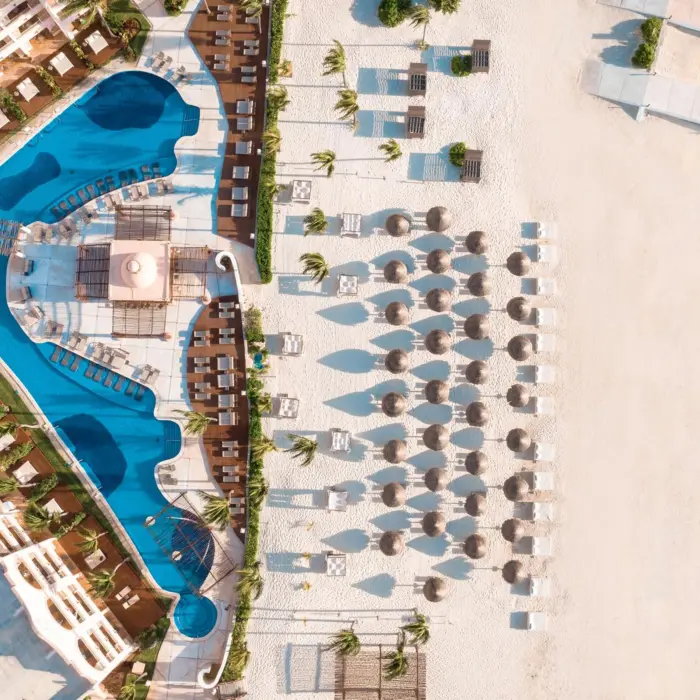 Aerial view of beachfront resort with pools, palapas, lounge chairs, and white sand meeting the turquoise Caribbean.