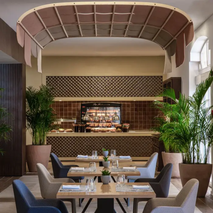 Elegant buffet restaurant with modern decor, potted plants, and neatly arranged dining tables with natural lighting.