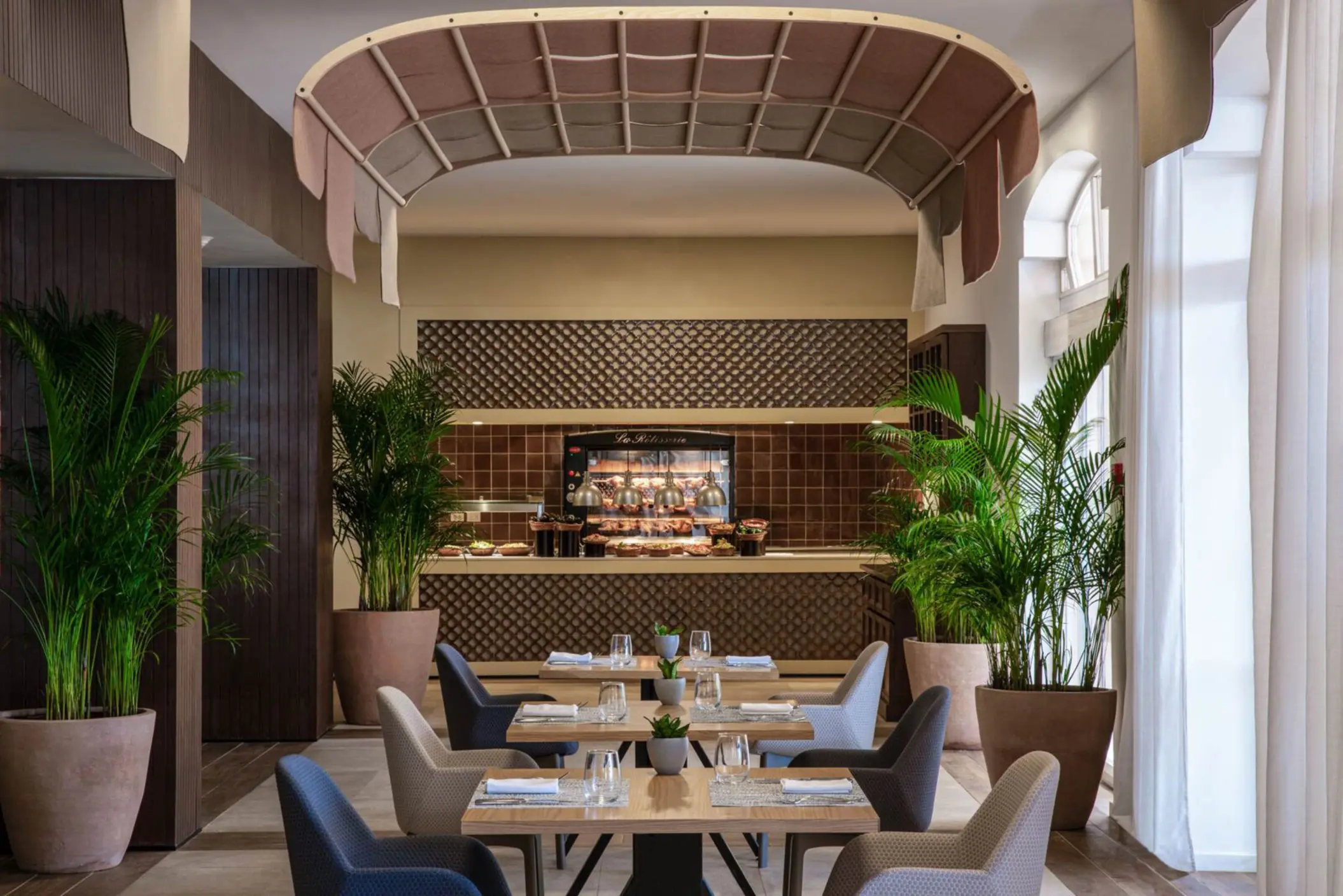 Elegant buffet restaurant with modern decor, potted plants, and neatly arranged dining tables with natural lighting.