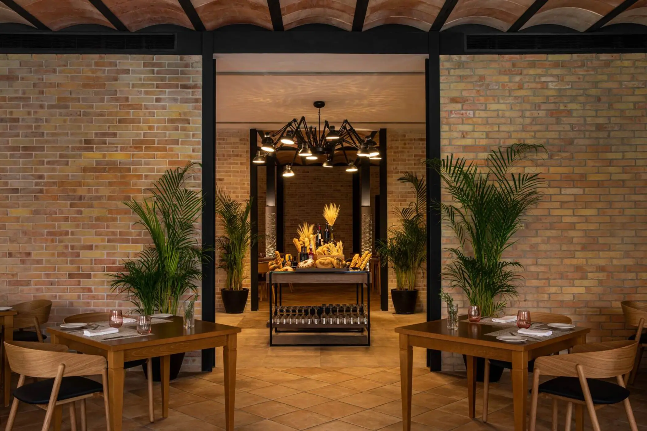 Cozy upscale steakhouse with brick walls, warm lighting, rustic wooden tables, and a gourmet bread station display.
