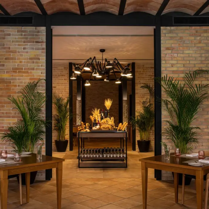 Cozy upscale steakhouse with brick walls, warm lighting, rustic wooden tables, and a gourmet bread station display.