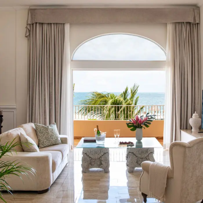 Spacious oceanview living room suite with upscale decor, elegant furnishings, and balcony overlooking tropical sea.