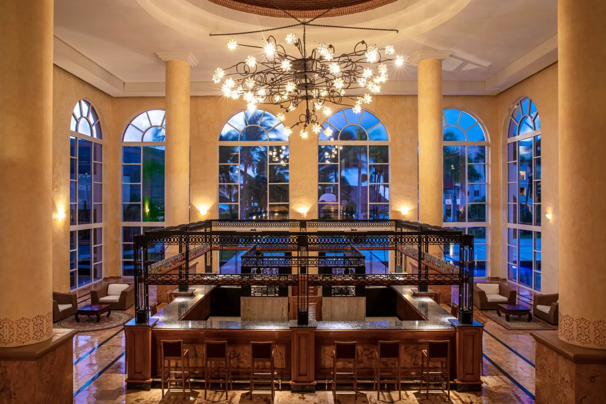 Sophisticated resort lobby bar with high ceilings, arched windows, modern chandelier, and elegant seating area.