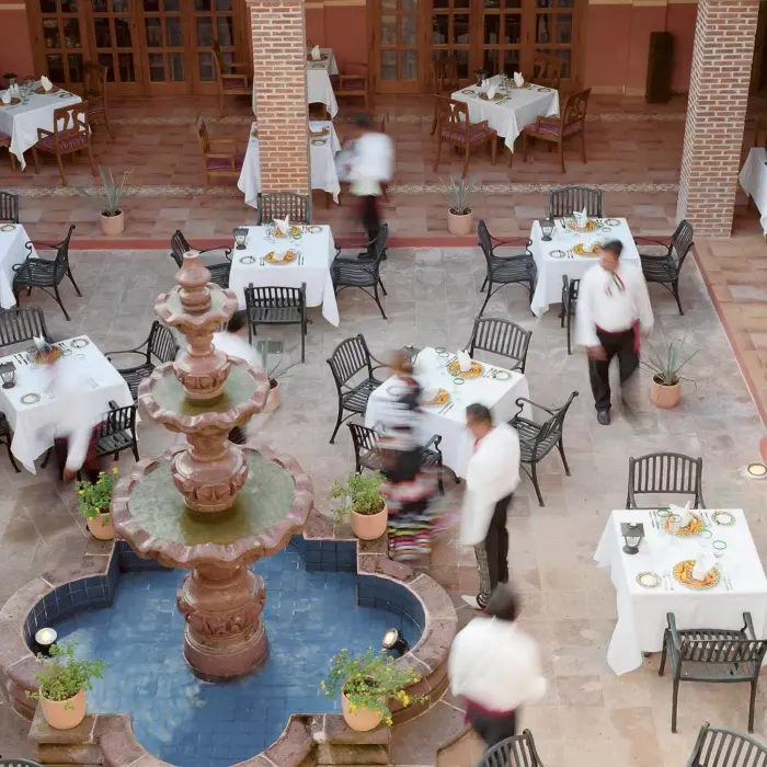 Open-air Mexican courtyard restaurant with fountain centerpiece, iron chairs, and brick archways.