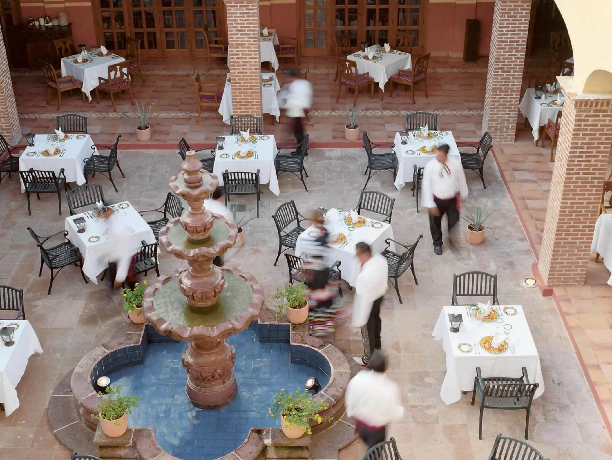Open-air Mexican courtyard restaurant with fountain centerpiece, iron chairs, and brick archways.