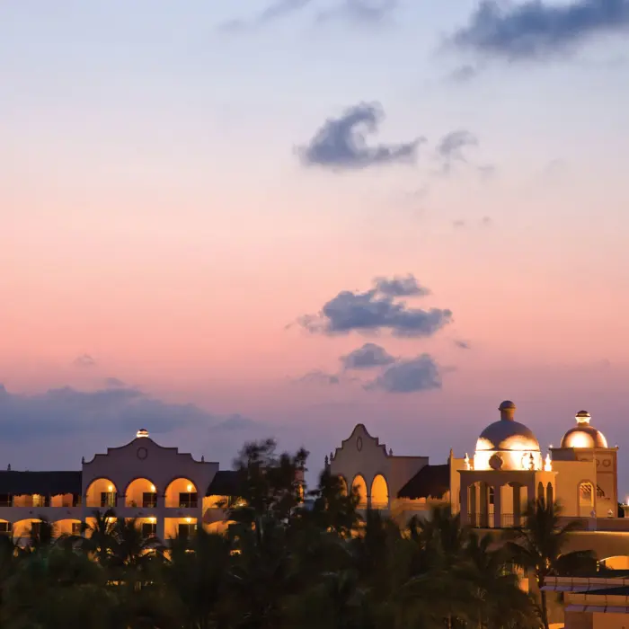 Romantic adults-only resort with winding pools, palm trees, and glowing buildings at twilight in Riviera Maya.