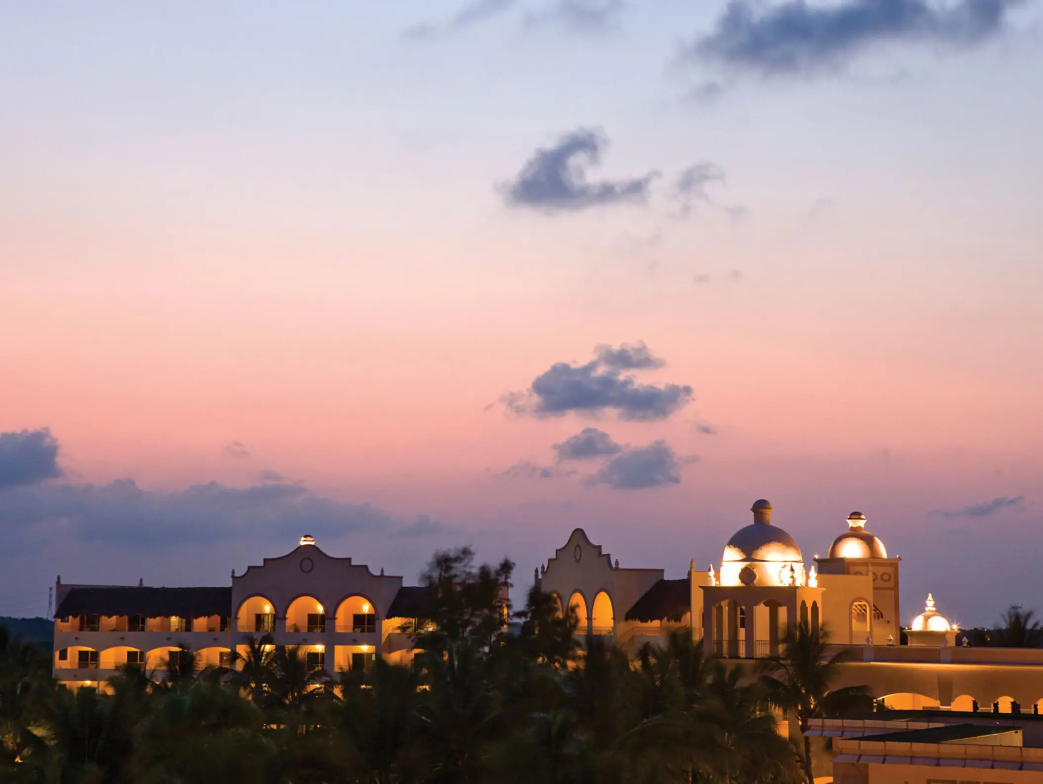 Romantic adults-only resort with winding pools, palm trees, and glowing buildings at twilight in Riviera Maya.