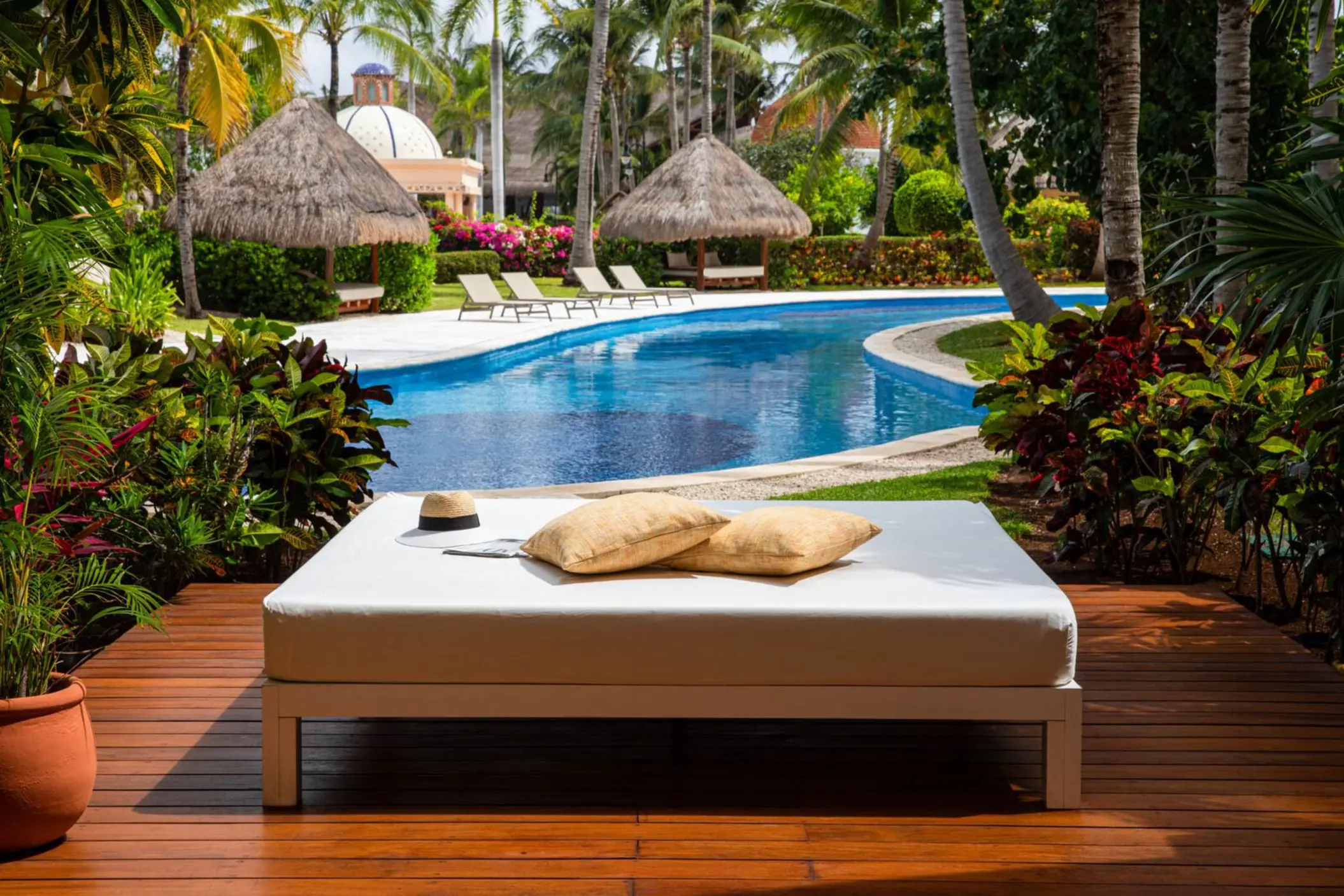 Poolside daybed surrounded by lush greenery and tropical palapas near a quiet swim-up suite area.