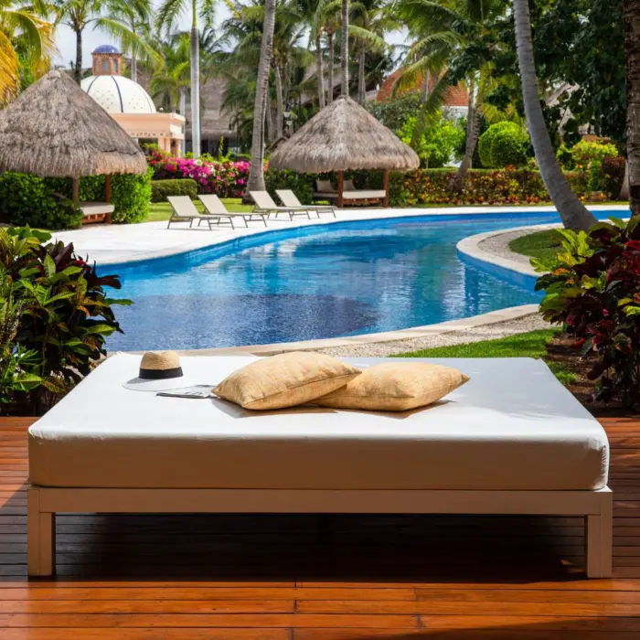Poolside daybed surrounded by lush greenery and tropical palapas near a quiet swim-up suite area.