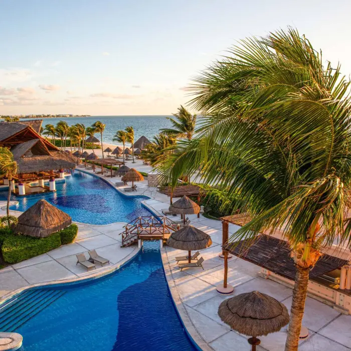 Beachfront infinity pool with palapa umbrellas, wooden bridges, and Caribbean views during golden hour.