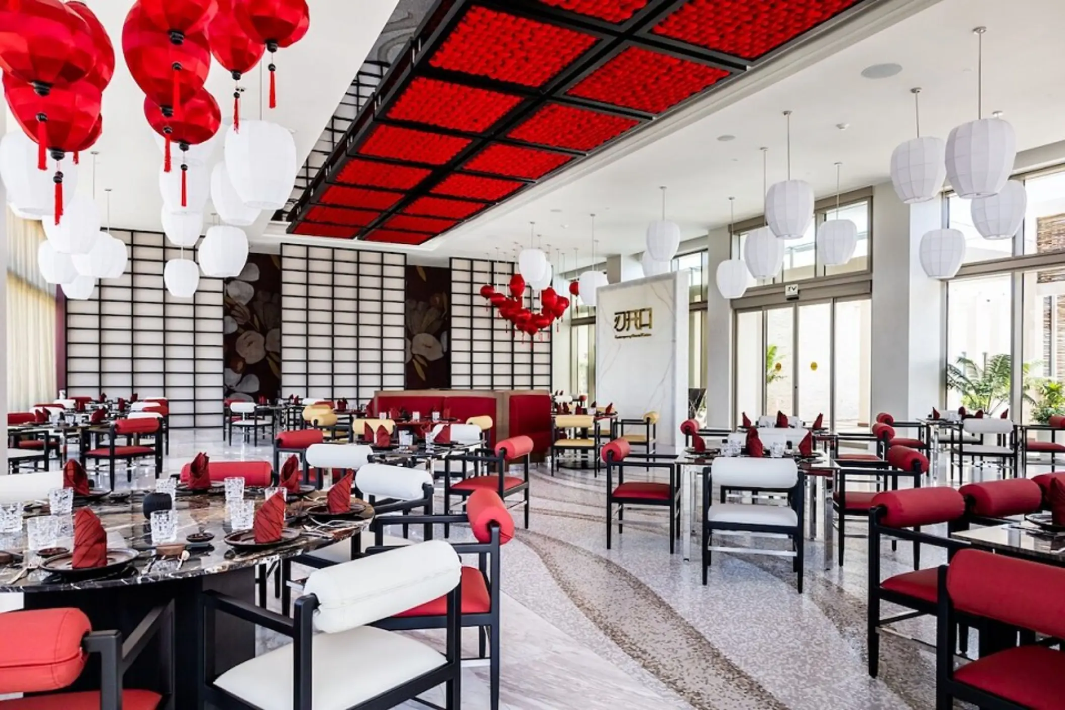 Modern Asian-inspired restaurant with red and white lanterns, bold ceiling design, and black marble tables.