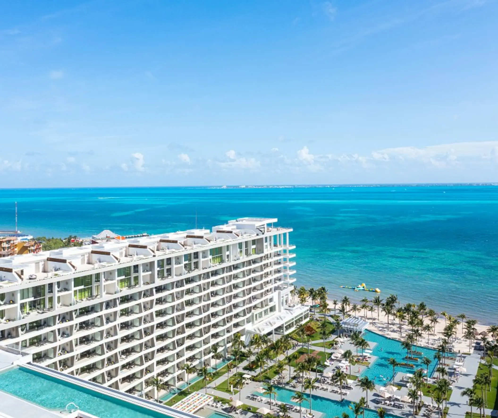 Aerial view of white sand beach, turquoise water, and palm-lined resort with curved beachfront walkways.
