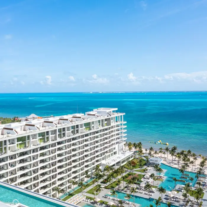 Aerial view of white sand beach, turquoise water, and palm-lined resort with curved beachfront walkways.