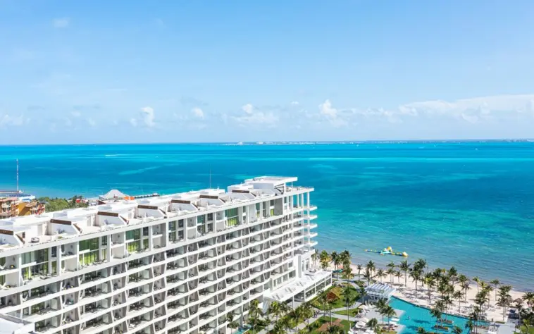 Aerial view of white sand beach, turquoise water, and palm-lined resort with curved beachfront walkways.