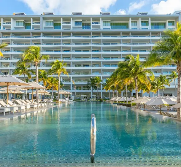 Large beachfront pool area with shallow walk-in edge, palm-lined terrace.
