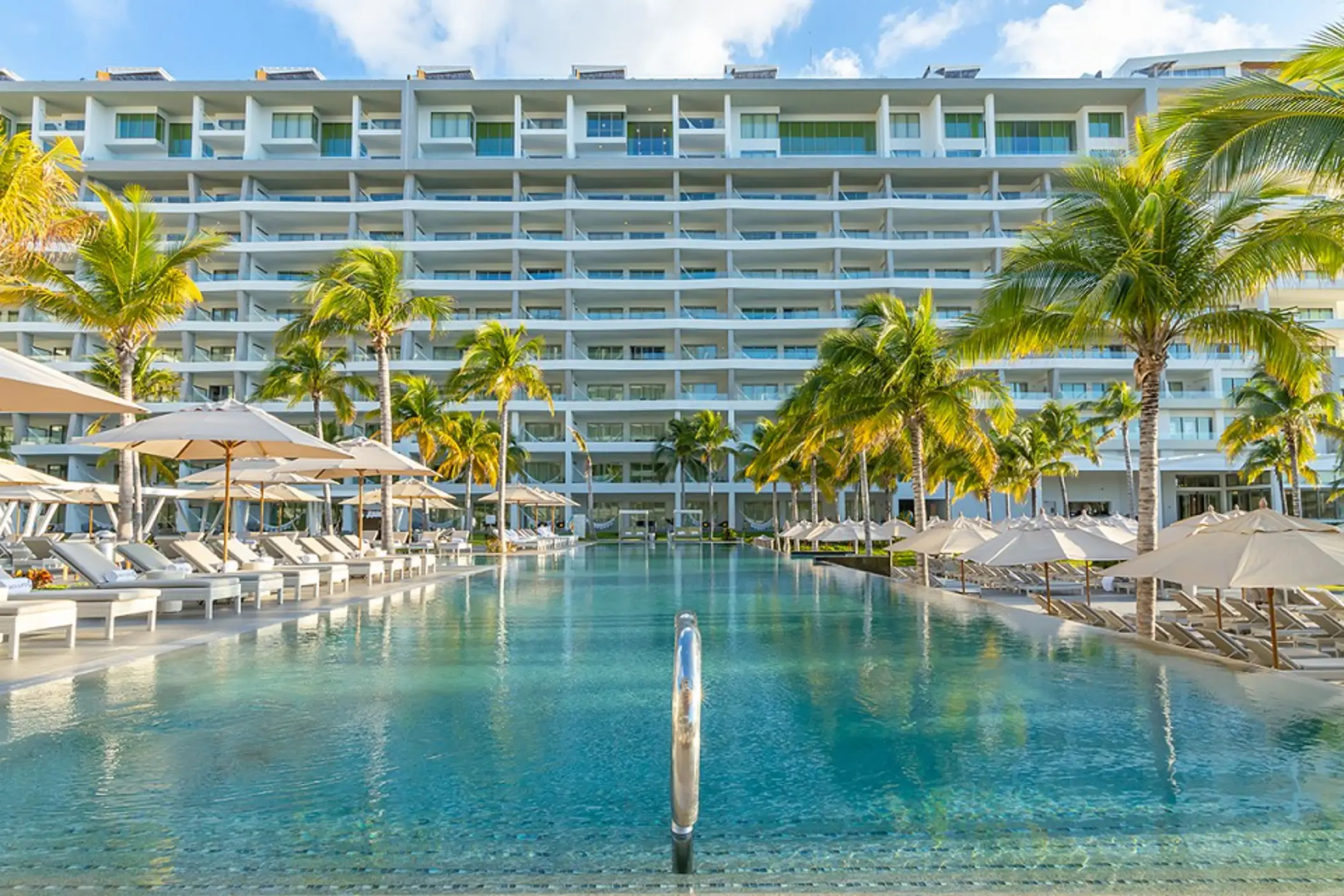 Large beachfront pool area with shallow walk-in edge, palm-lined terrace.