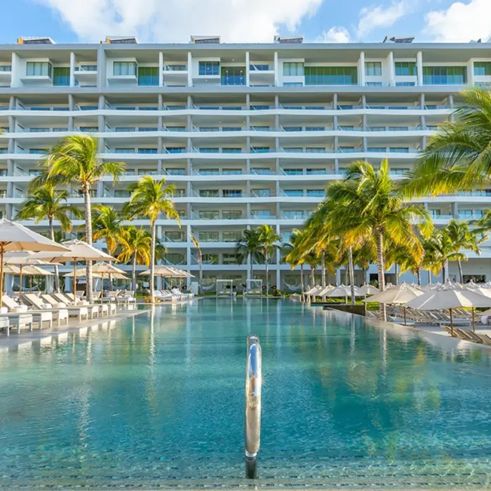 Large beachfront pool area with shallow walk-in edge, palm-lined terrace.