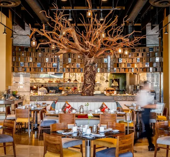 Upscale restaurant with a dramatic sculpted tree centerpiece, open kitchen, and cozy wood-accented dining setup.