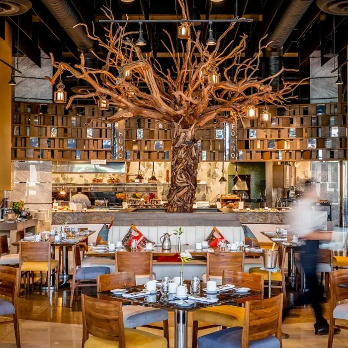 Upscale restaurant with a dramatic sculpted tree centerpiece, open kitchen, and cozy wood-accented dining setup.