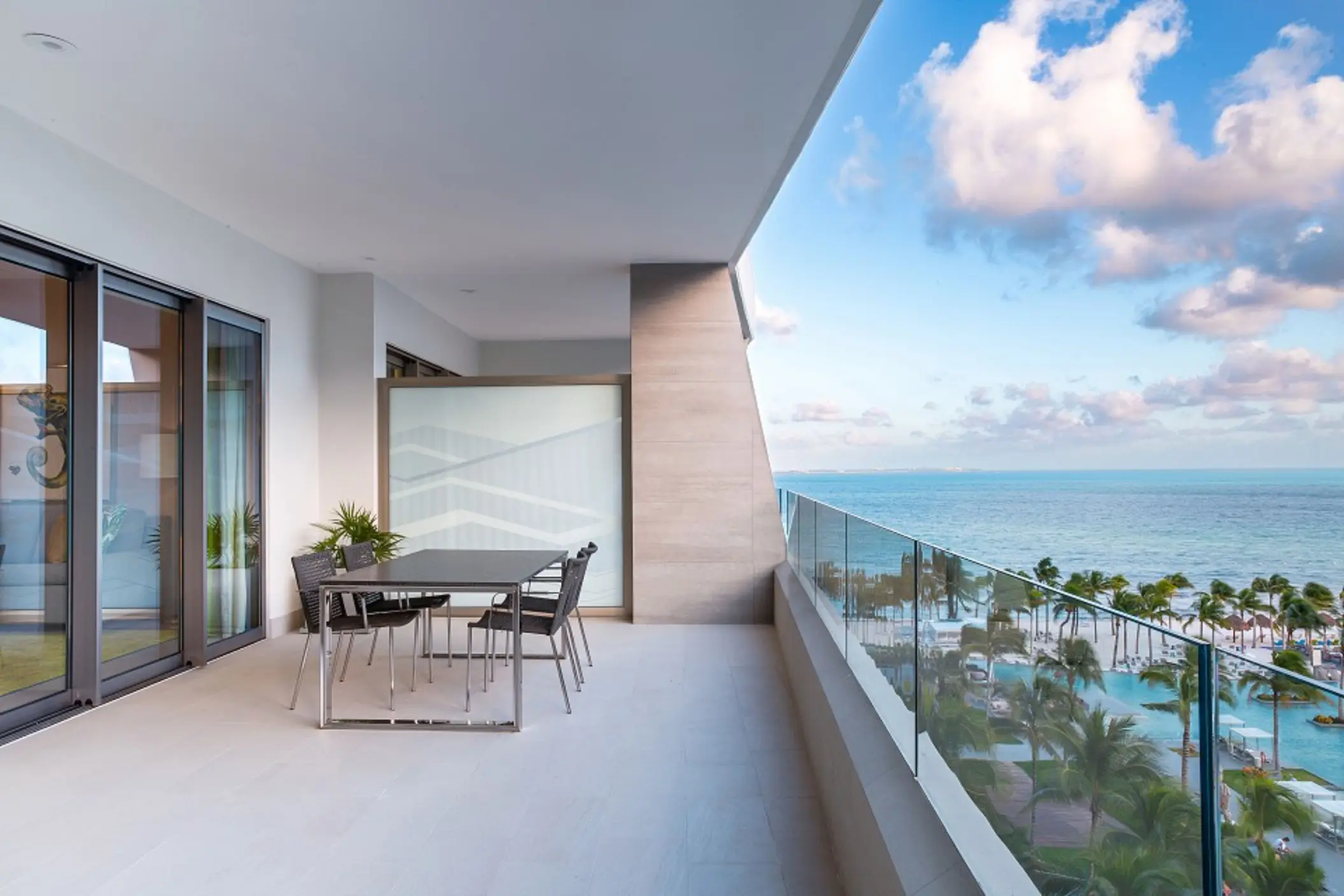 Spacious ocean-view terrace with glass railing, outdoor dining table, and panoramic beach and pool views.