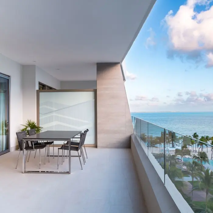 Spacious ocean-view terrace with glass railing, outdoor dining table, and panoramic beach and pool views.