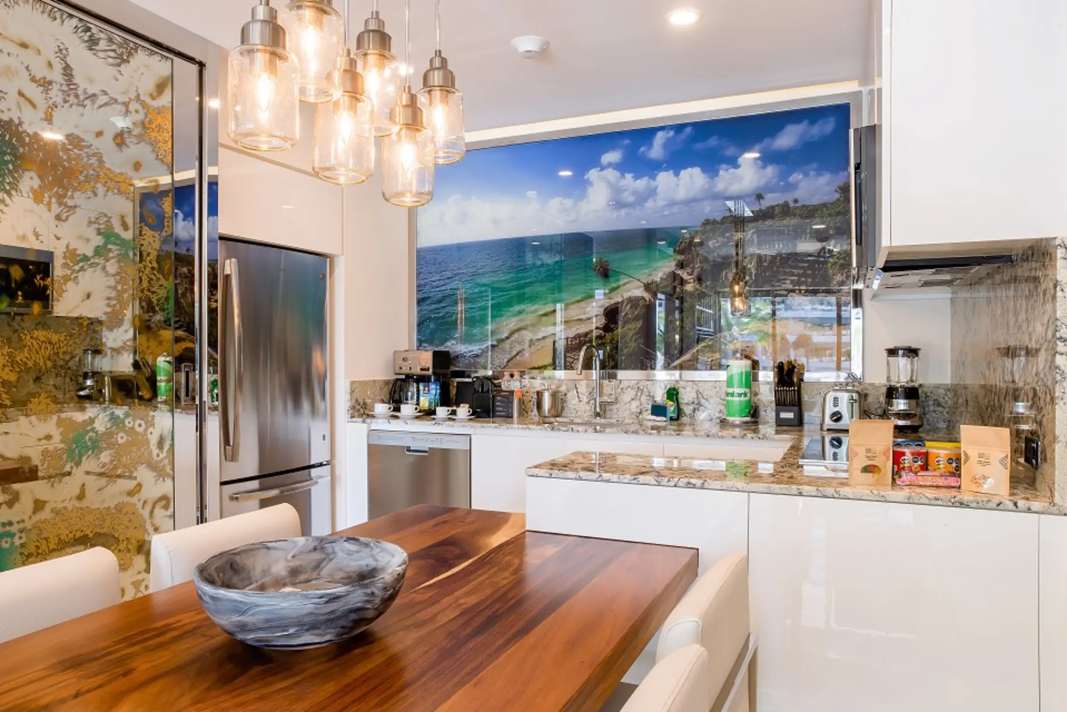 Modern kitchen with wood dining table, pendant lights, granite countertops, and ocean-themed wall art.