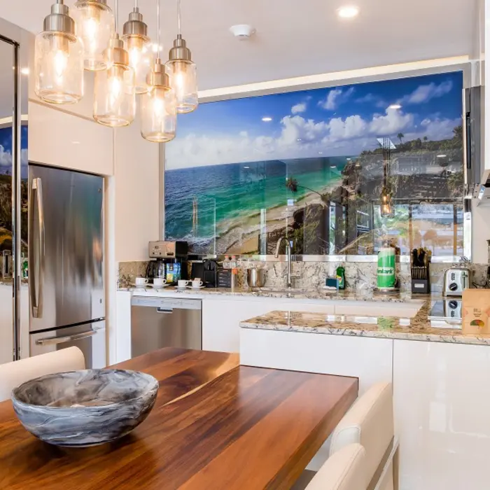 Modern kitchen with wood dining table, pendant lights, granite countertops, and ocean-themed wall art.