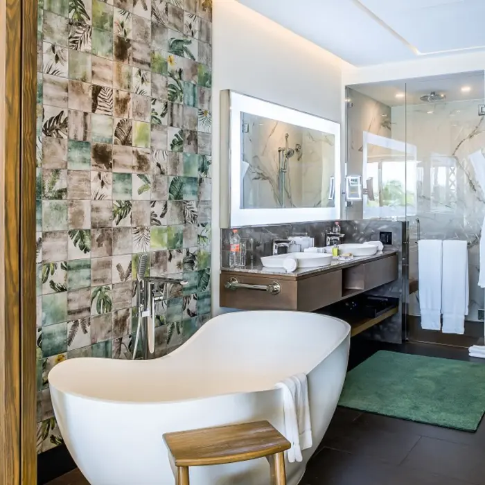 Luxury bathroom with freestanding tub, rainforest-themed tile wall, double vanity, and glass-enclosed shower.