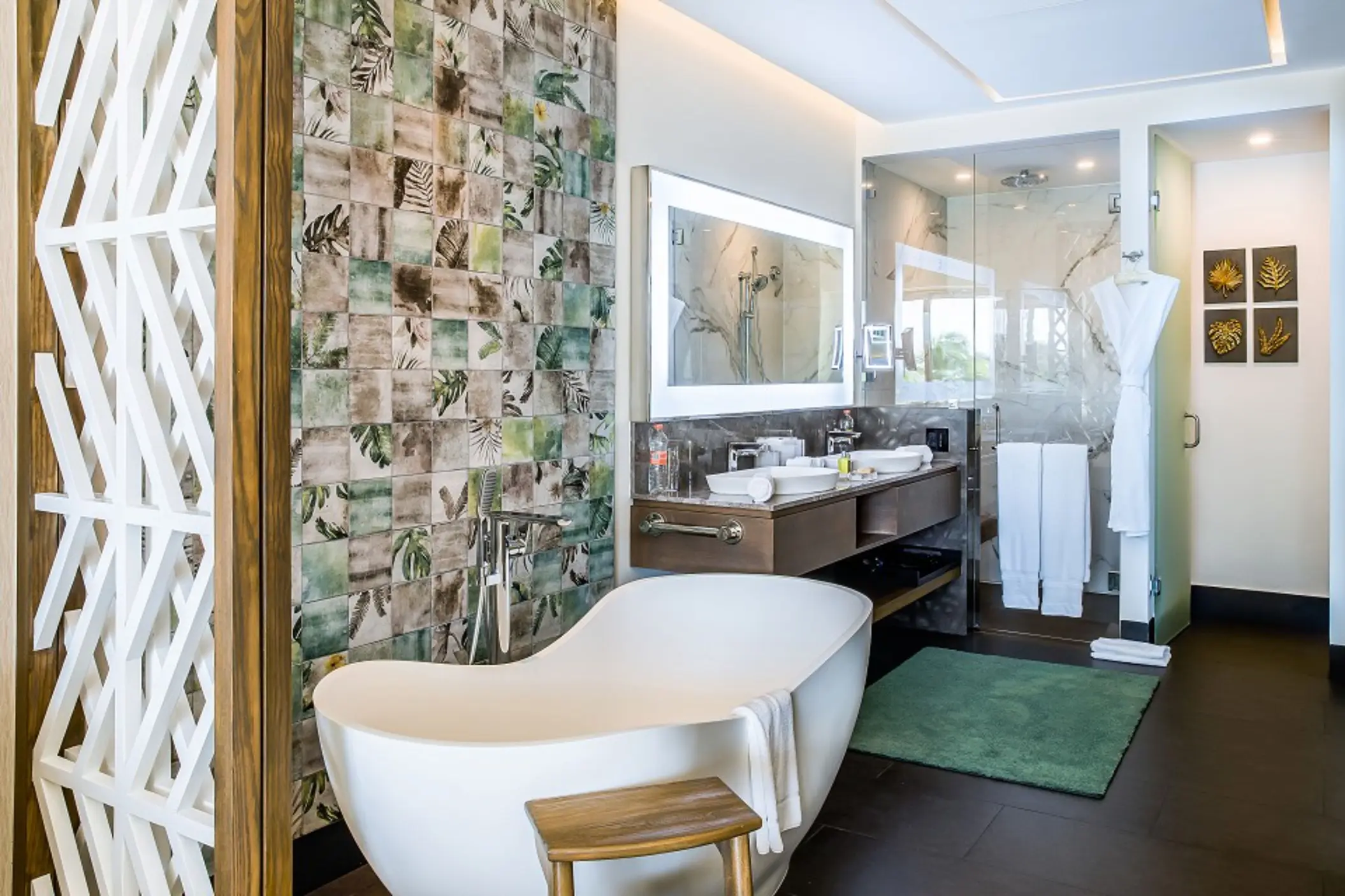 Luxury bathroom with freestanding tub, rainforest-themed tile wall, double vanity, and glass-enclosed shower.