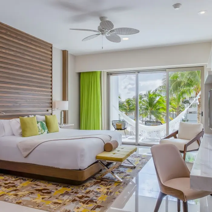 Elegant bedroom with king bed, tropical pillows, hammock on balcony, and view of lush palm trees outside.