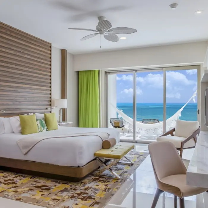Bright oceanview Junior Suite with a king bed, seating area, and balcony overlooking turquoise waters.