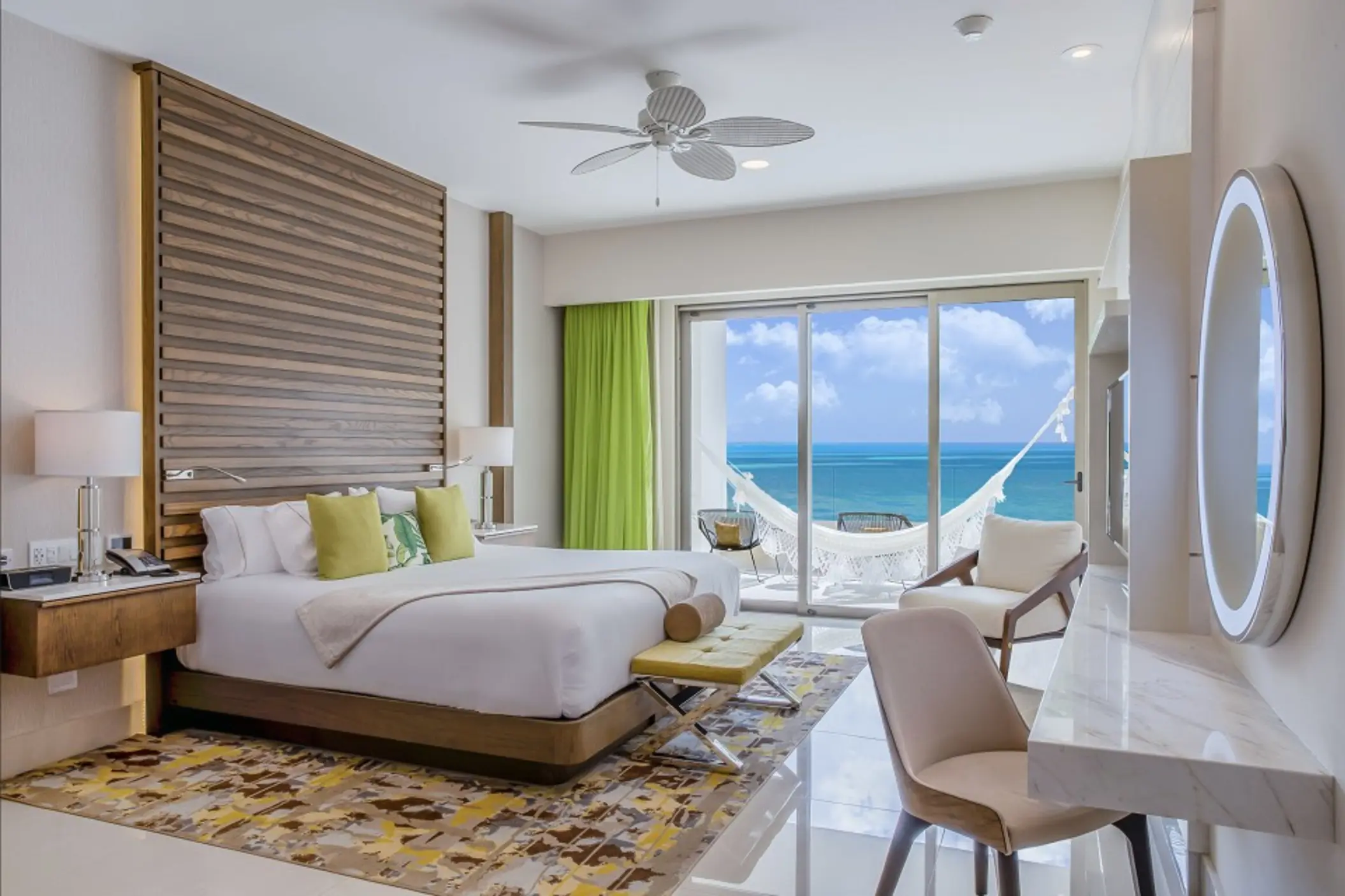 Bright oceanview Junior Suite with a king bed, seating area, and balcony overlooking turquoise waters.