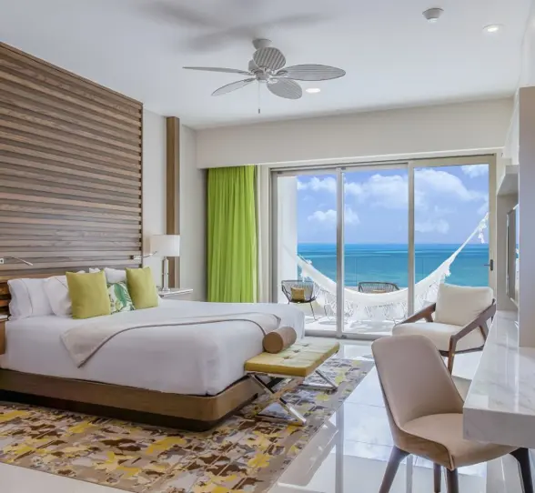Bright oceanview Junior Suite with a king bed, seating area, and balcony overlooking turquoise waters.