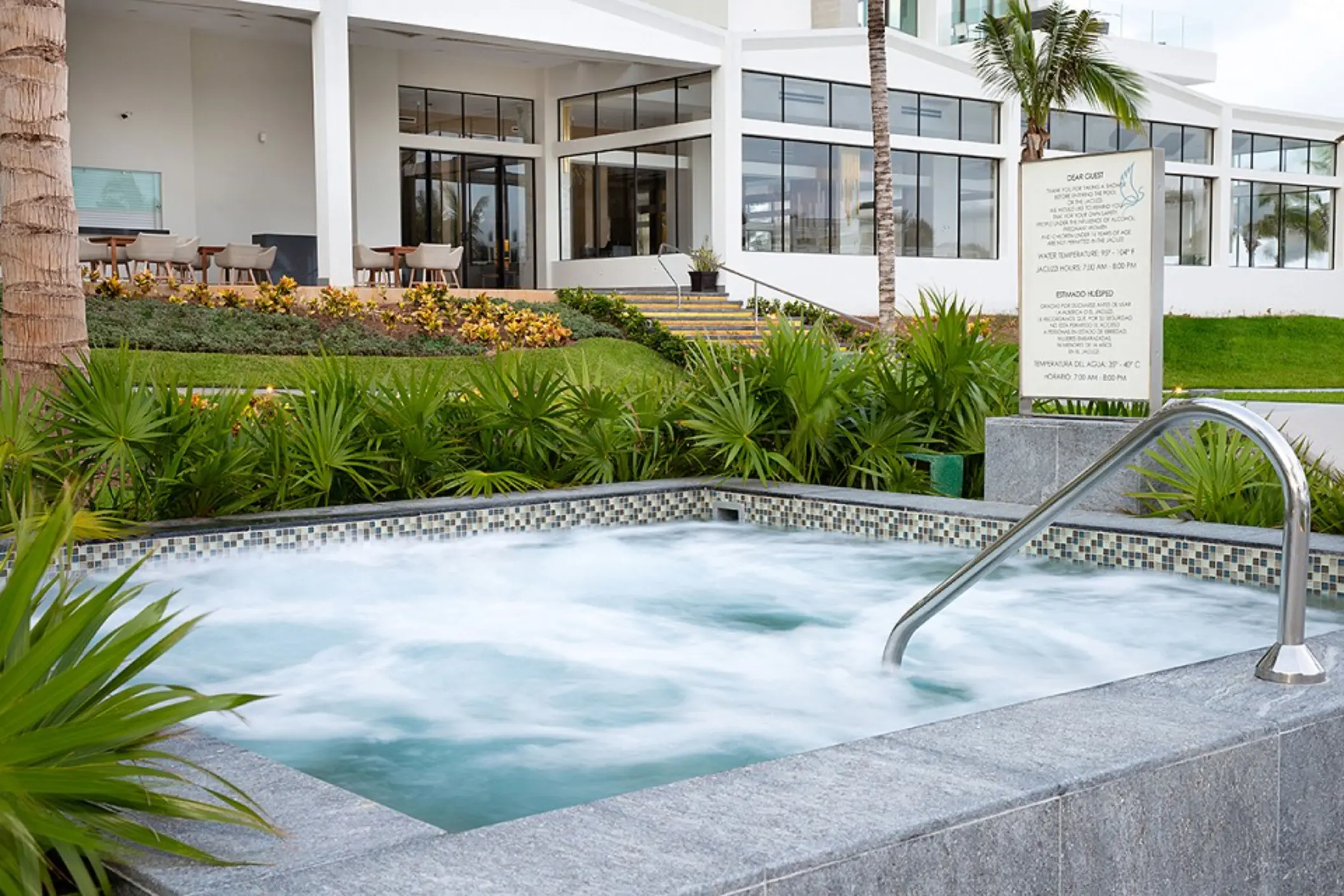 Large infinity pool surrounded by palm trees, cabanas, and sun loungers facing the ocean.