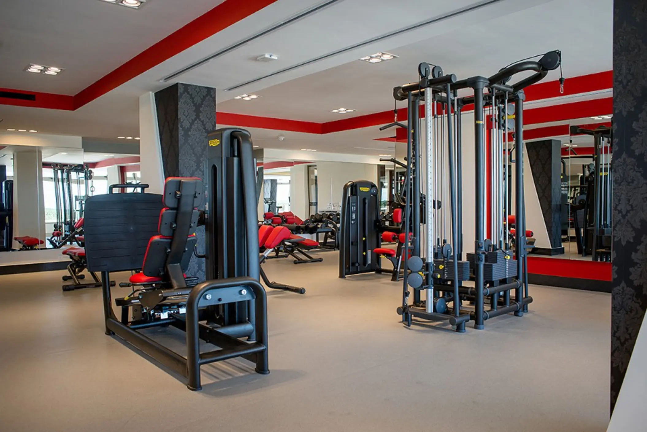 Open gym space with cardio equipment, resistance machines, and tropical greenery visible through the windows.