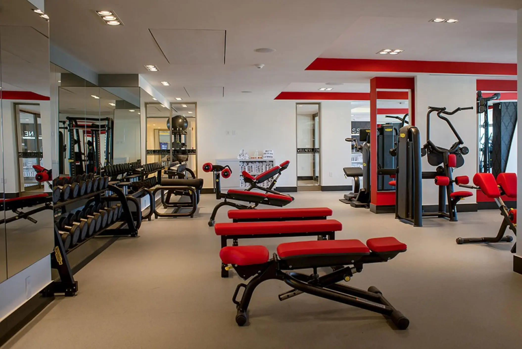 Fitness area with weights, kettlebells, and mirrors, set in a bright space with sleek flooring and lighting.